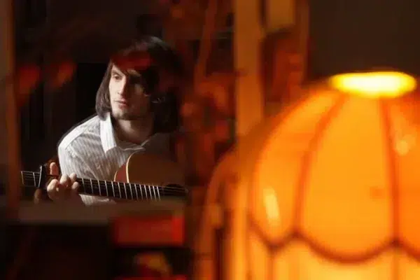 guy-playing-guitar-with-orange-old-fashioned-lampshade-in-foreground