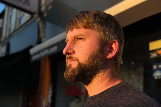 man-close-up-face-in-golden-light-wearing-dark-jumper-looking-off-into-distance-in-street