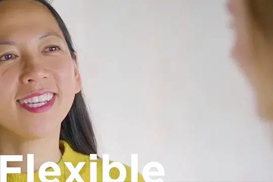 asian-woman-smiling-at-worker-wearing-yellow-jumper-and-pink-lipstick-the-white-word-flexible-at-bottom-left