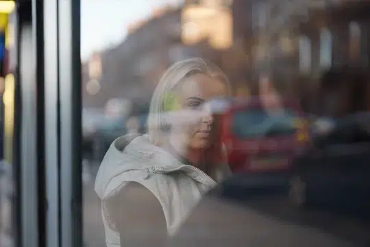 a-blonde-haired-women-seen-through-a-window-listening-to-her-friend-with-the-reflection-of-the-street-on-the-glass