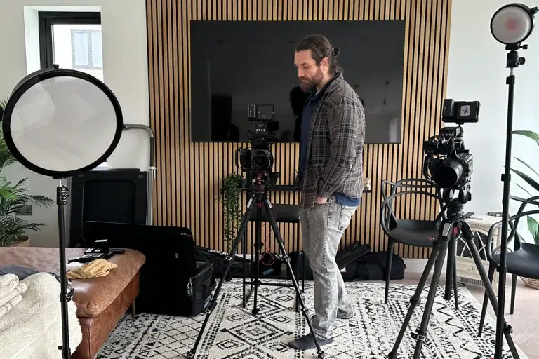 interview-filming-set-up-with-2-x-camcorders-2-lights-and-man-with-beard-and-ponytail-casually-dressed-standing-between-them
