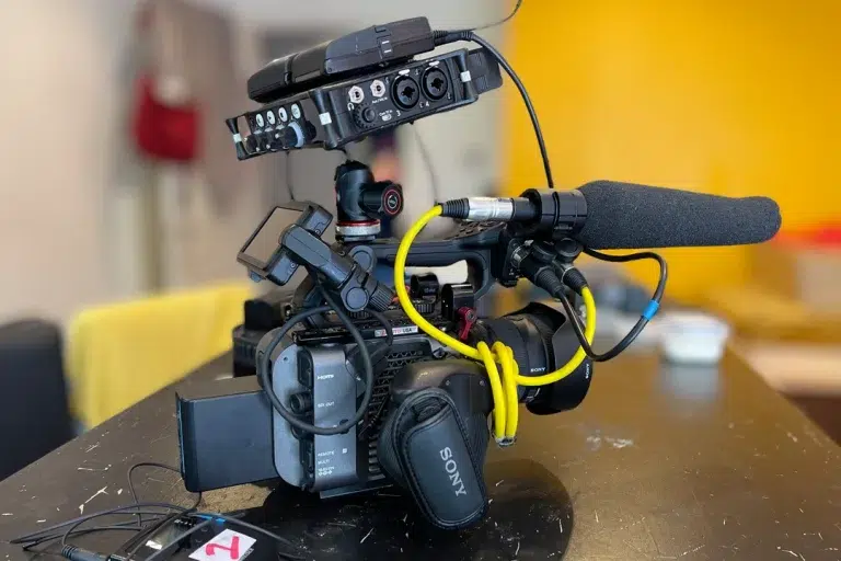 sony-fx6-mic-and-yellow-audio-cable-with-battery-and-monitor-sitting-ontable-top-blurry-backdrop